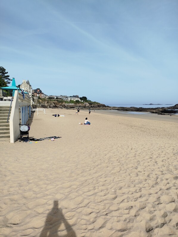 Ein Strand mit einer Treppe, die zu einem Gebäude führt, einem Kinderwagen und einer Person, die im Sand sitzt.