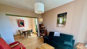 Una sala de estar con un sofá verde, una mesa de centro de madera, un sillón rojo y un comedor con una mesa y sillas.