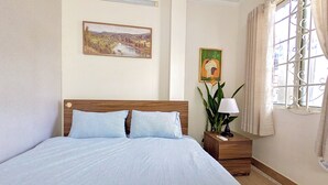 Een slaapkamer met een houten bed, een nachtkastje met een lamp, een schilderij en een raam met gordijnen.