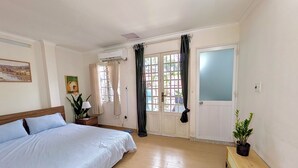 Een slaapkamer met een bed, een nachtkastje, een kamerplant, een raam met gordijnen en een airconditioning.