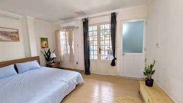 A bedroom with a bed, a bedside table, a potted plant, a window with curtains, and an air conditioning unit.