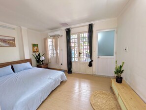Un dormitorio con cama, mesita de noche, planta en maceta, ventana con cortinas y aire acondicionado.