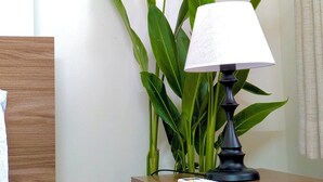 Een opgemaakt bed, een nachtkastje met een lamp, een afstandsbediening en een schilderij aan de muur.