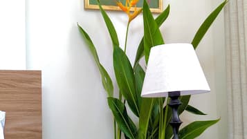 A neatly made bed, a bedside table with a lamp, a remote control, and a painting on the wall.