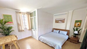 Een slaapkamer met een bed, een houten tafel, een stoel, een raam met gordijnen en een wand met een lijst eromheen.