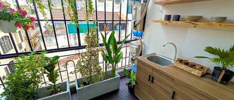 Varanda com plantas em vasos, um armário de madeira e vista para a rua.