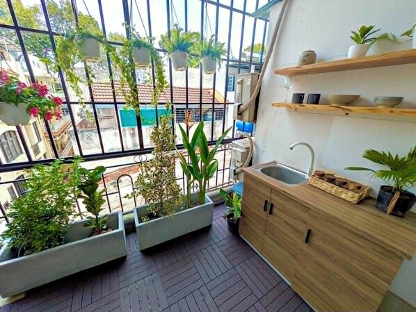 Un balcón con plantas en macetas, un mueble de madera y vista a la calle.