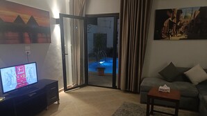 Un soggiorno con televisione, un divano, un tavolino da caffè e una porta scorrevole in vetro che dà su una zona piscina.