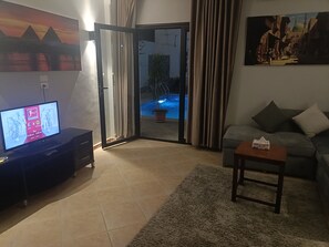 Una sala de estar con televisor, sofá, mesa de centro y puerta corrediza de vidrio que da a una zona de piscina.