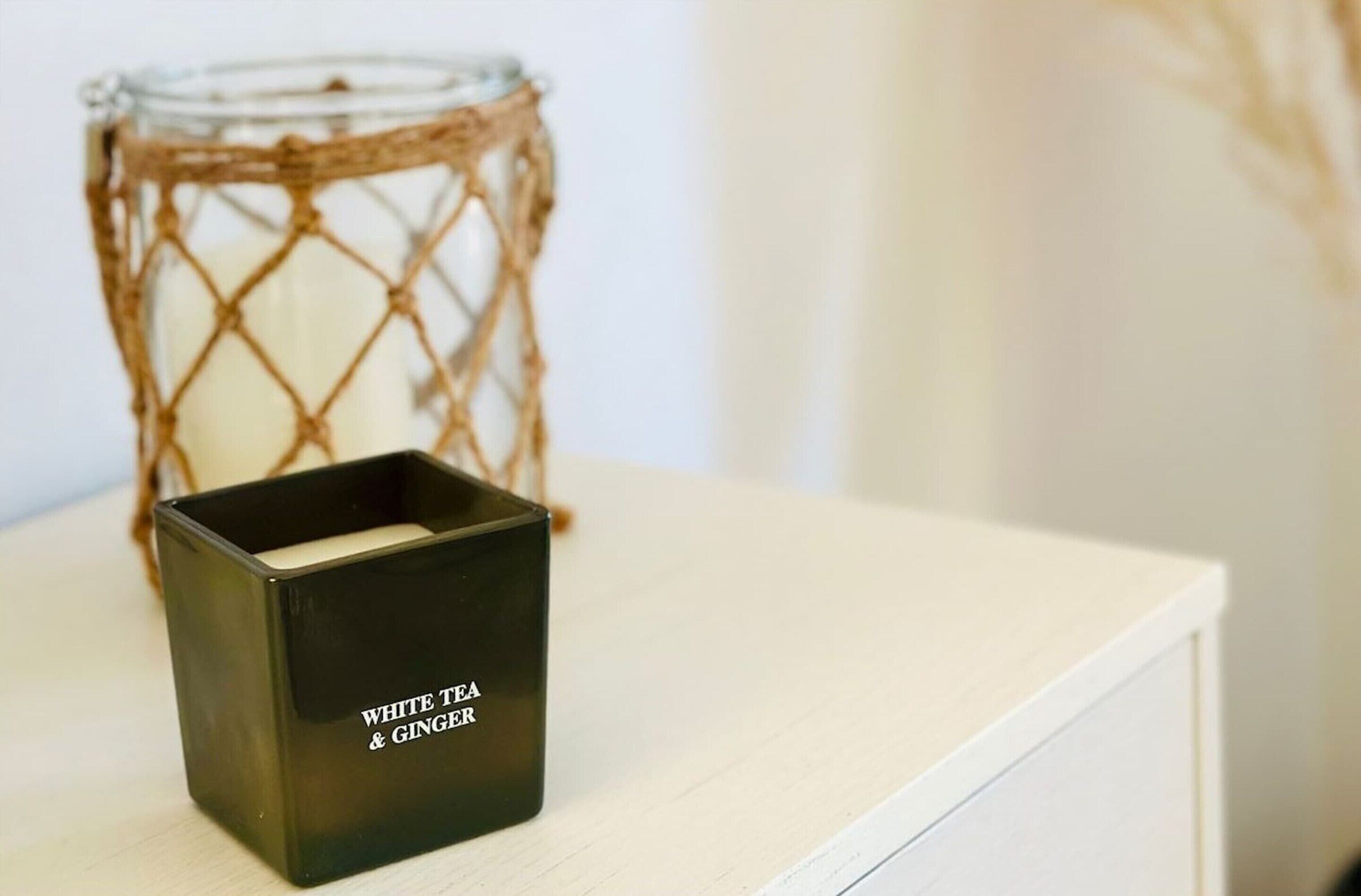 Una vela en una caja negra con la etiqueta 'WHITE TEA & GINGER' sobre una superficie blanca.