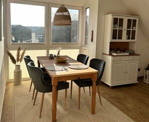 Un comedor con una mesa de madera, sillas negras, una lámpara colgante y un armario blanco con puertas de cristal.
