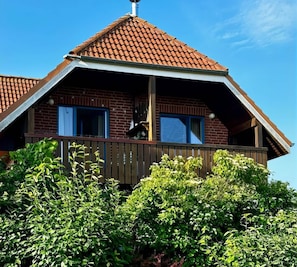A two-story building with a red-tiled roof, a wooden balcony, and brick walls. - Ferienwohnung in Lemkenhafen auf Fehmarn (Fehmarn)