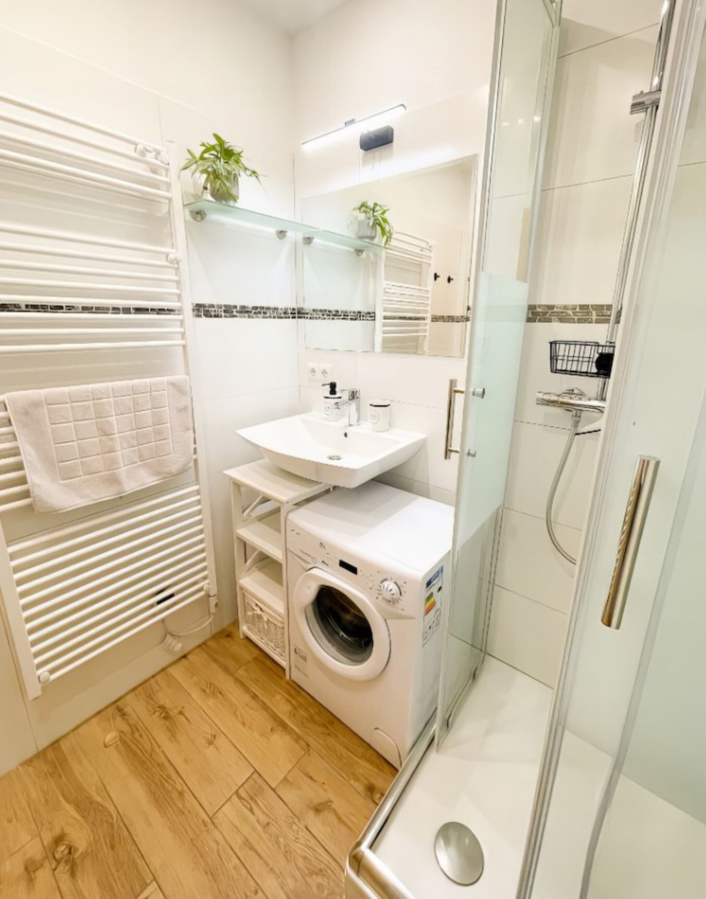 A modern bathroom with a built-in washing machine, a glass shower enclosure, and a white sink with a mirror above.