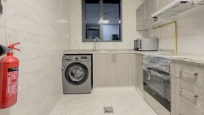 Eine kleine Küche mit Waschmaschine, Mikrowelle und Backofen, einem Feuerlöscher und einem Fenster.