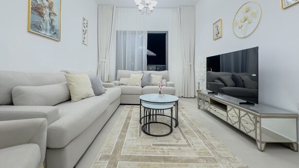 Ein modernes Wohnzimmer mit einem Ecksofa, einem runden Couchtisch, einem Fernseher auf einer Kommode und Kunstwerken an den Wänden.
