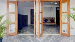 Une pièce avec un parquet à motifs en chevrons, un canapé avec des coussins et un ventilateur fixé au mur.