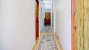 Un couloir aux murs blancs, doté d’un sol carrelé et de portes en bois.