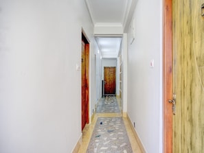 A hallway with white walls, a tiled floor, and wooden doors. - Super Deluxe Room 55 Pillars House (Shillong)
