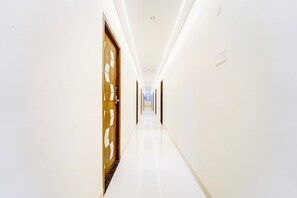 A long, narrow hallway with white walls and a glossy floor, leading to a door with a geometric pattern. - Deluxe Room Super Hotel O Aarapalayam (Madurai)