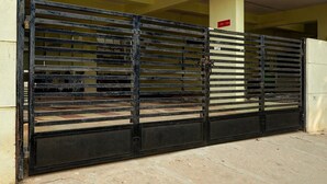 A metal gate with horizontal bars, a yellow wall, and a red sign. - Deluxeurban Drift (Bengaluru)