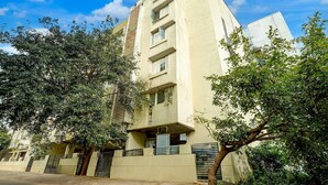 A multi-story residential building with balconies, a flat roof, and trees in the foreground. - Deluxeurban Drift (Bengaluru)