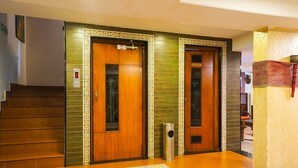 A hotel lobby with two wooden doors, a staircase, and a trash bin. - Super Townhouse Oak Prabhat Road (Pune)