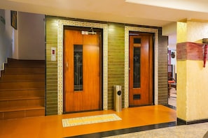 Eine Hotelhalle mit zwei Holztüren, einer Treppe und einem Mülleimer.