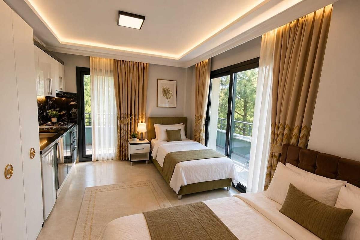 Una habitación de hotel moderna con una cama grande, una mesita de noche pequeña, una lámpara de noche y un ventanal con cortinas, que ofrece vistas a zonas verdes.