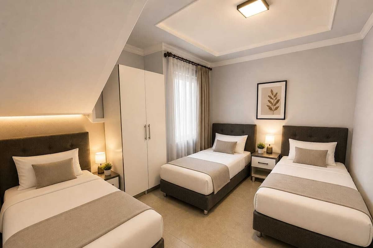 Habitación de hotel con dos camas, un armario, una mesita de noche con lámpara y una obra de arte enmarcada en la pared.