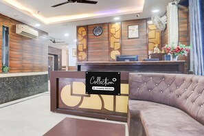 Un espace d’accueil comprenant une horloge, un comptoir de réception, un canapé et un climatiseur fixé au mur.
