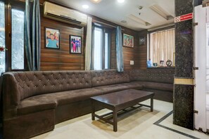 A brown leather sofa, a wooden coffee table, and a 'No Smoking' sign in a room with wooden paneling and large windows. - Classic With Balconymahipalpur Near Airport (New Delhi)