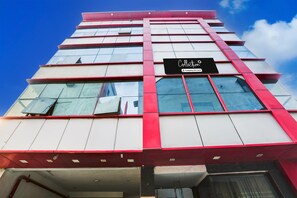 A multi-story building with a prominent red and white facade, large windows, and a sign indicating a company service. - Classic With Balconymahipalpur Near Airport (New Delhi)