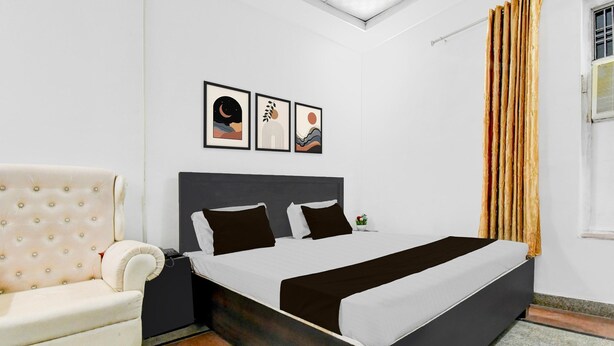A bedroom with a bed, a sofa, a nightstand, and a window with curtains. - Deluxe Khusboo Palace (Lucknow)