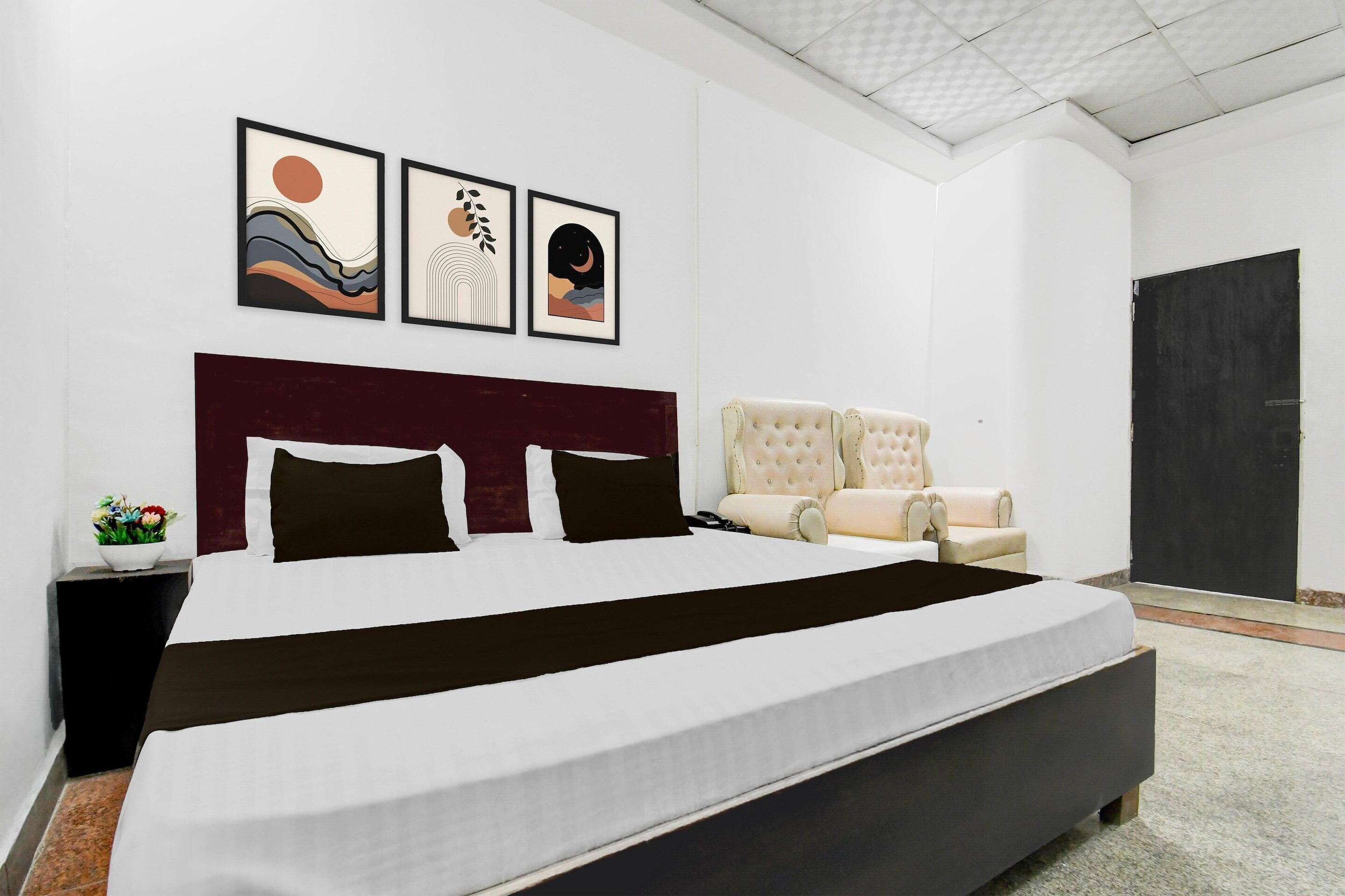 A modern bedroom with a large bed, a headboard, a chaise lounge, and three framed artworks on the wall.