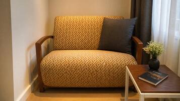 A sofa with a geometric pattern, a dark cushion, and a small table with a book and a vase of flowers.