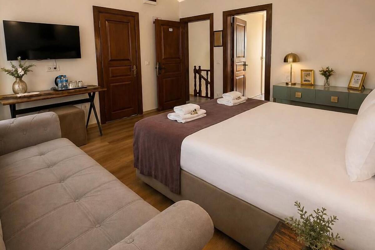 A hotel room with a bed, a sofa, a TV, a desk, and a mirror.