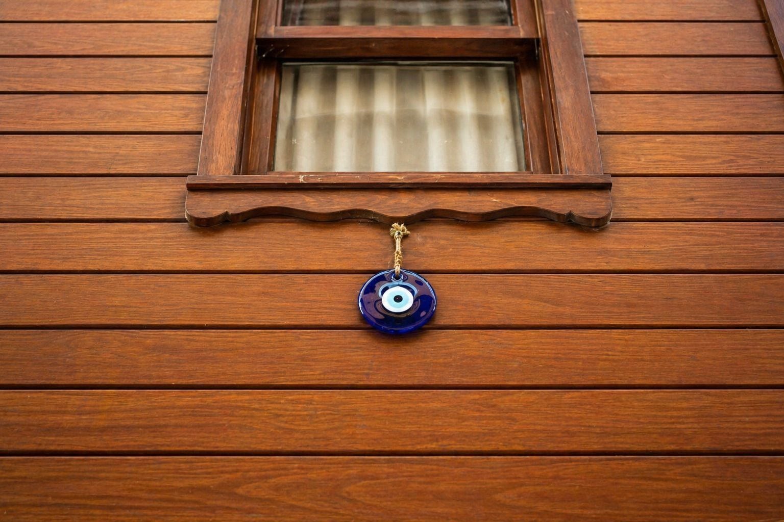A wooden wall with a window and a blue decorative item hanging below it.