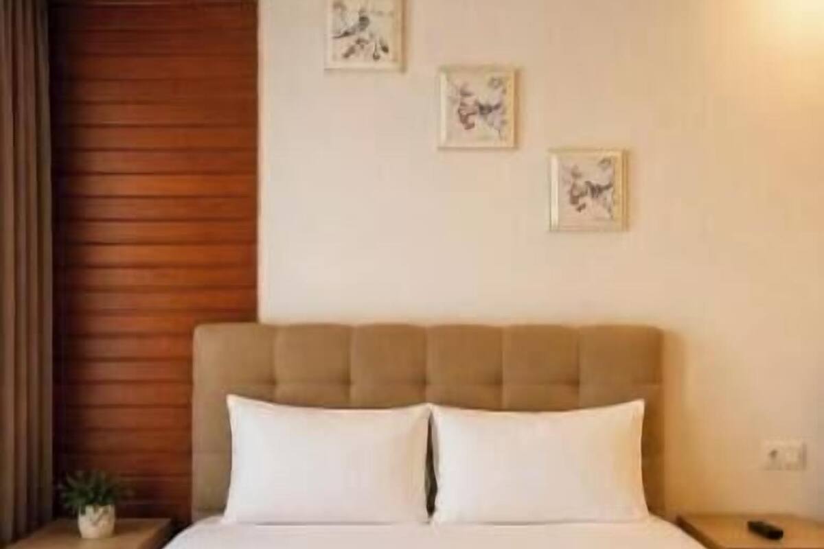 A hotel room with a bed, two pillows, a headboard, a nightstand, a remote control, and two towels.