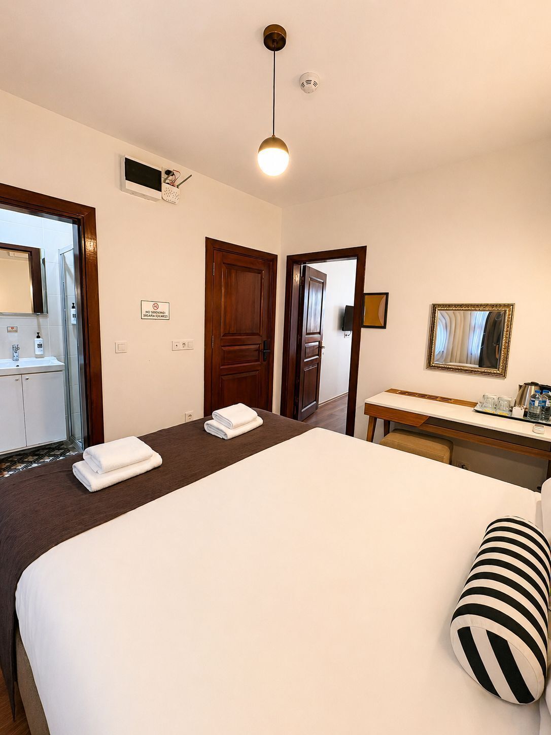 A hotel room with a bed, a desk, a mirror, and a bathroom visible through an open door.