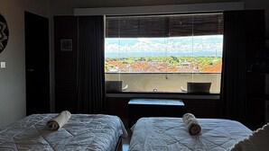 A room with two beds, a ceiling fan, a large window with a view of a landscape, and a door.