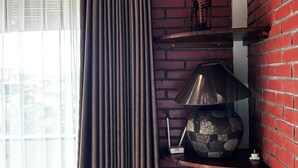 A room with a brick wall, a window with sheer curtains, and a shelf with a decorative item.