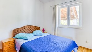 Ein Schlafzimmer mit einem Bett, einem Nachttisch, einem Fenster mit Vorhängen und einer Holzbalkendecke.