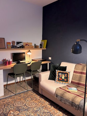 Un salon moderne avec un bureau, un ordinateur et un canapé agrémenté d’un coussin décoratif.