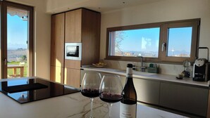 A kitchen with a wine bottle and glasses, a coffee machine, and a view of the countryside. - A dwelling where time slows down and regain the rhythm of nature. (Morrovalle)