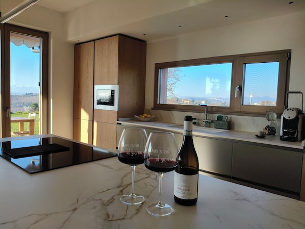 A kitchen with a wine bottle and glasses, a coffee machine, and a view of the countryside.