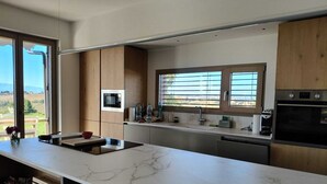 A modern kitchen with a marble countertop, wooden cabinets, a built-in oven, and a window with blinds. - A dwelling where time slows down and regain the rhythm of nature. (Morrovalle)