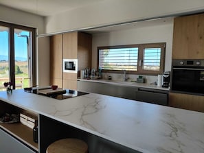 A modern kitchen with a marble countertop, wooden cabinets, a built-in oven, and a window with blinds.