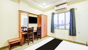 A hotel room with a bed, a desk with chairs, a TV, an air conditioning unit, and a window with curtains. - Super Deluxe Roomred Hills Sitara Grand (Hyderabad)