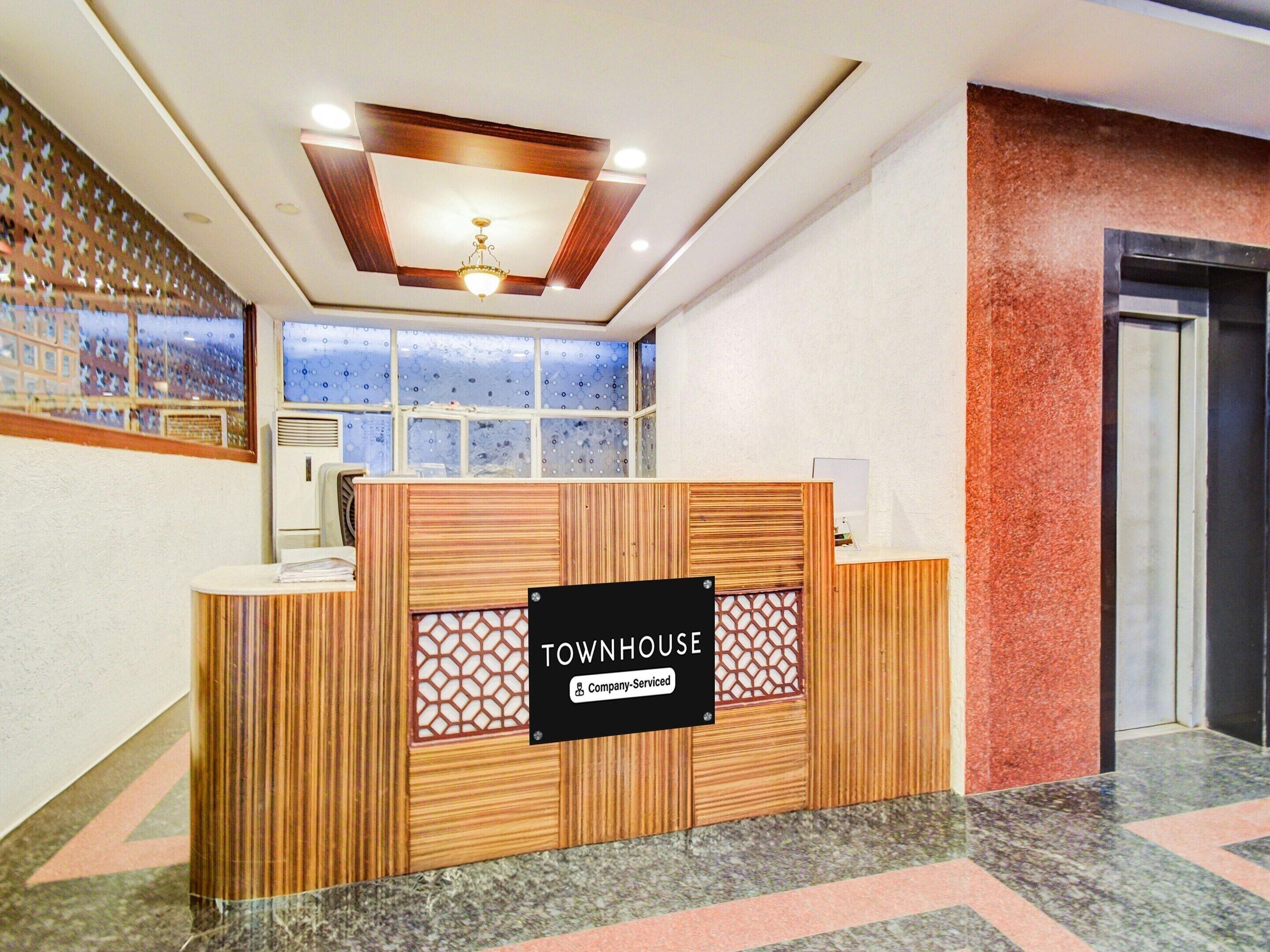 A reception desk with a sign reading 'TOWNHOUSE' and a company-serviced label. There is a ceiling fan, a window with a view, and a door to the right.