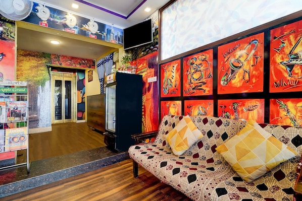A hotel lobby with a sofa, a TV, and colorful wall art.